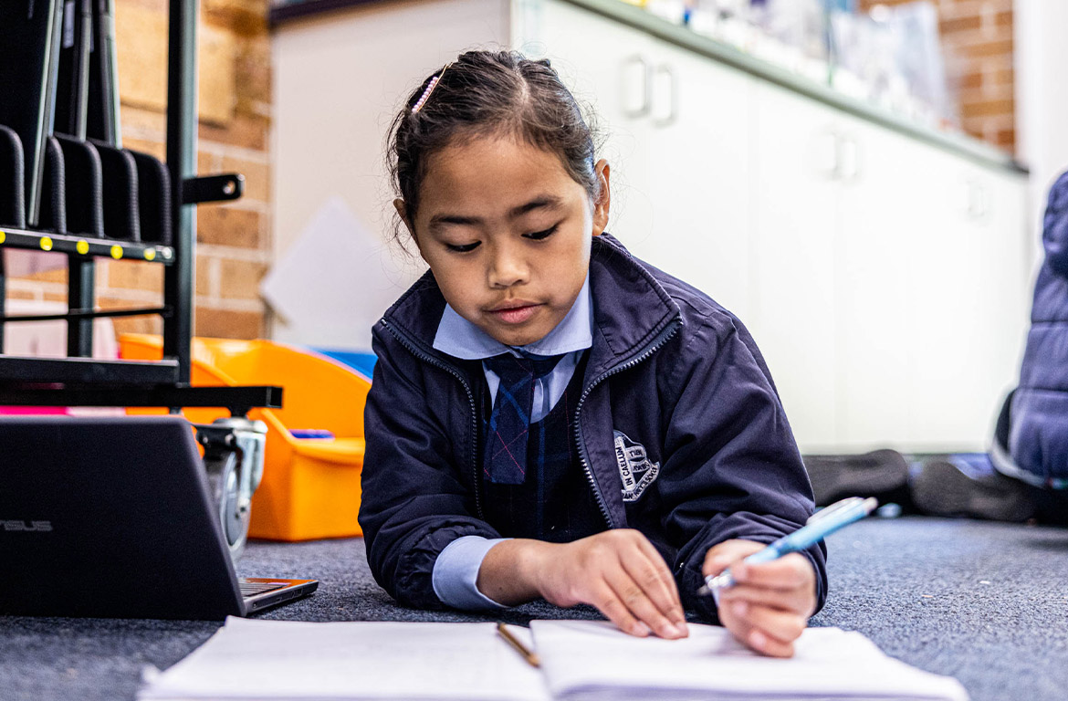 Student writing in her work book at St John Vianney's Primary School Doonside